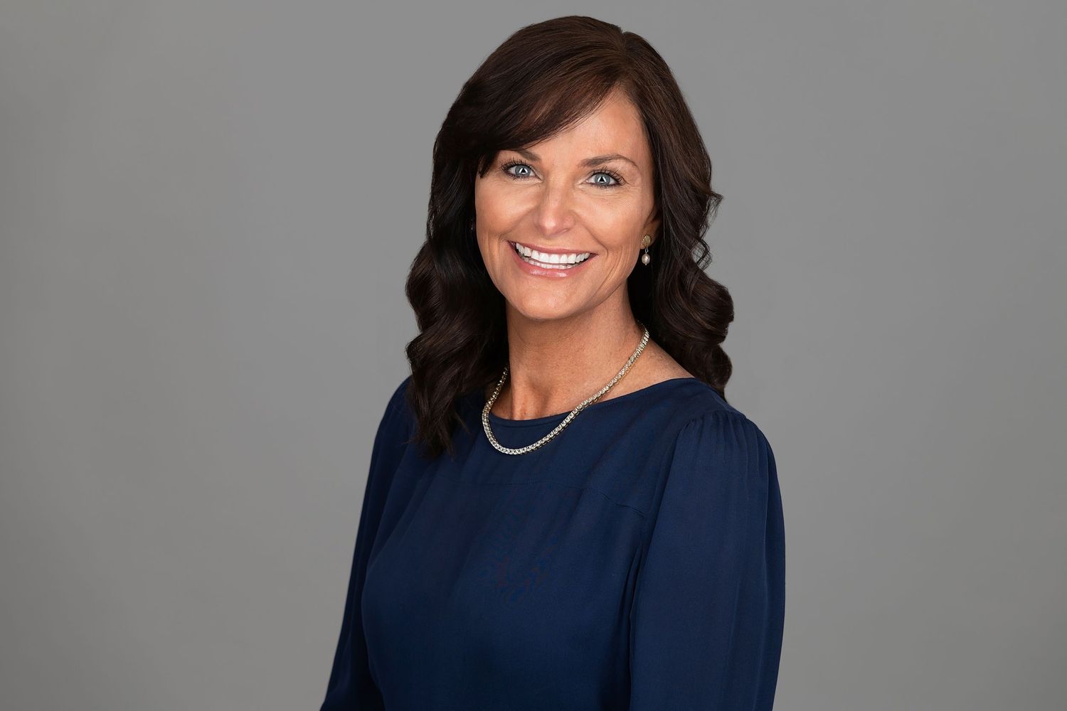 Professional headshot of woman in navy dress against gray background.