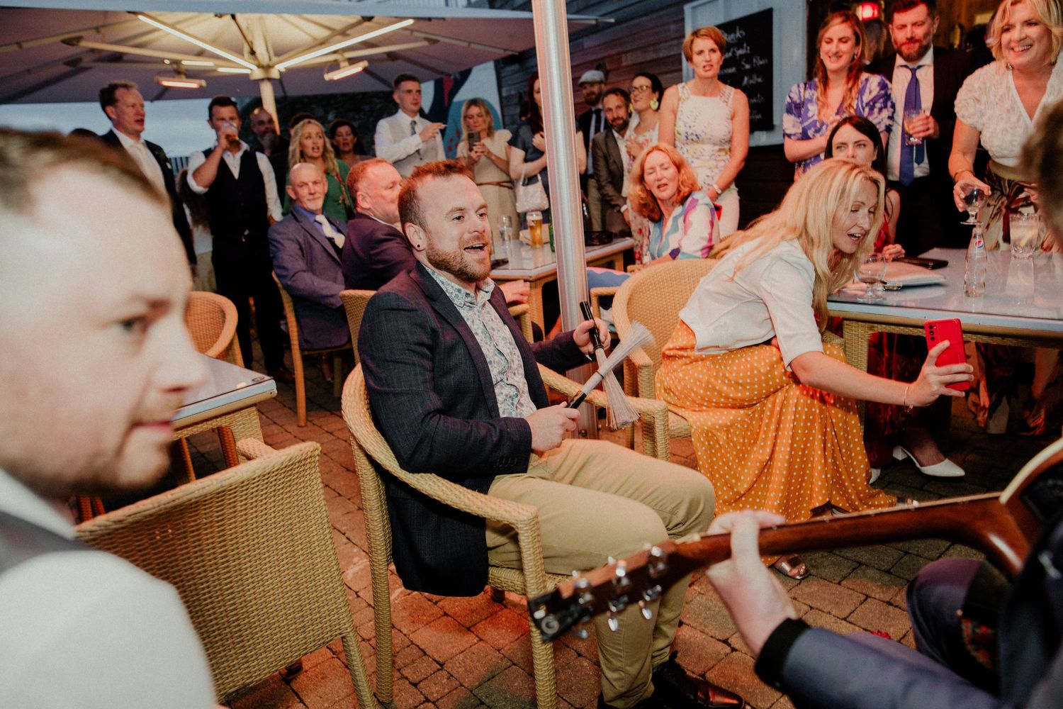 Wedding entertainment performs for guests seated under outdoor umbrellas.