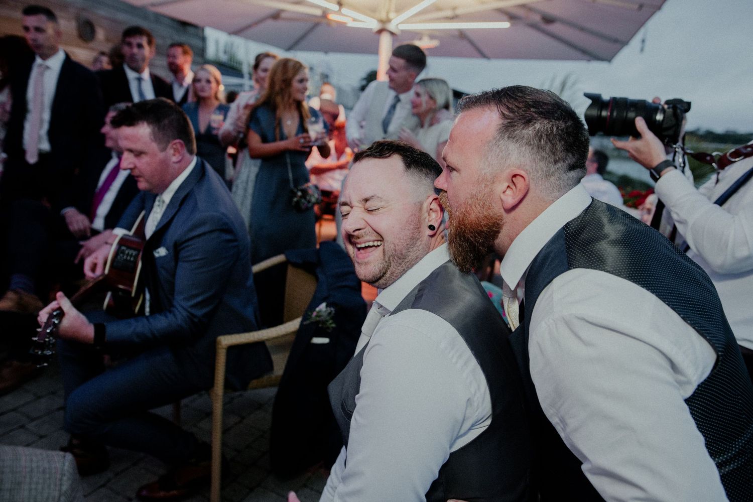 Party guests sharing laughter and joy during a wedding celebration under a tent.