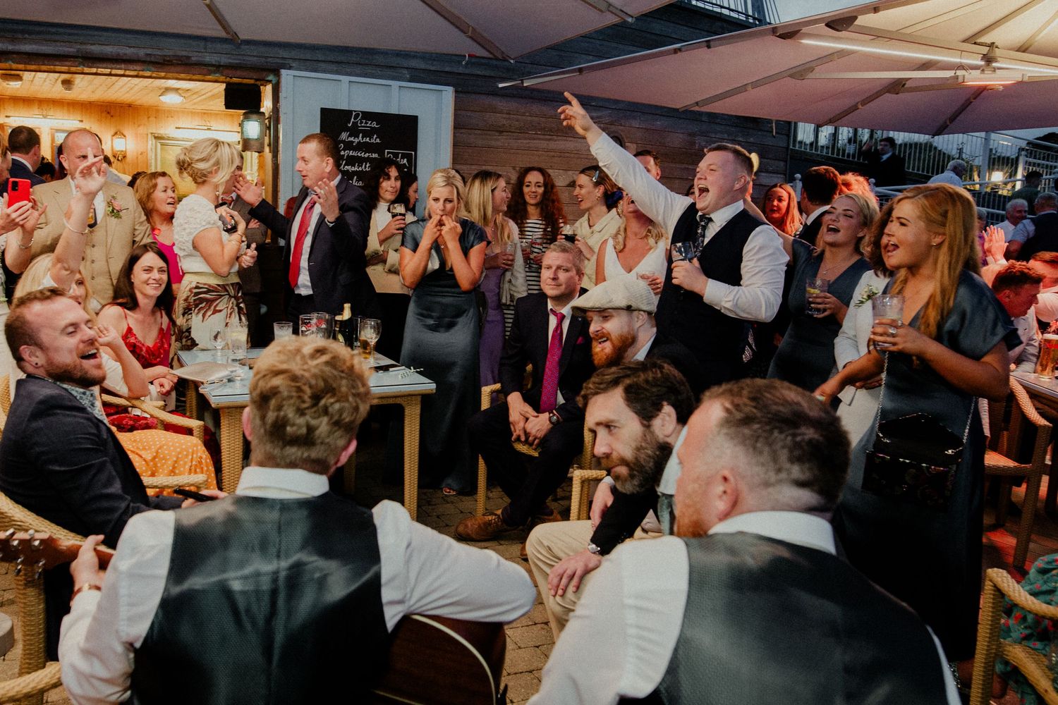 Crowded wedding reception with guests celebrating and clapping under an outdoor tent.