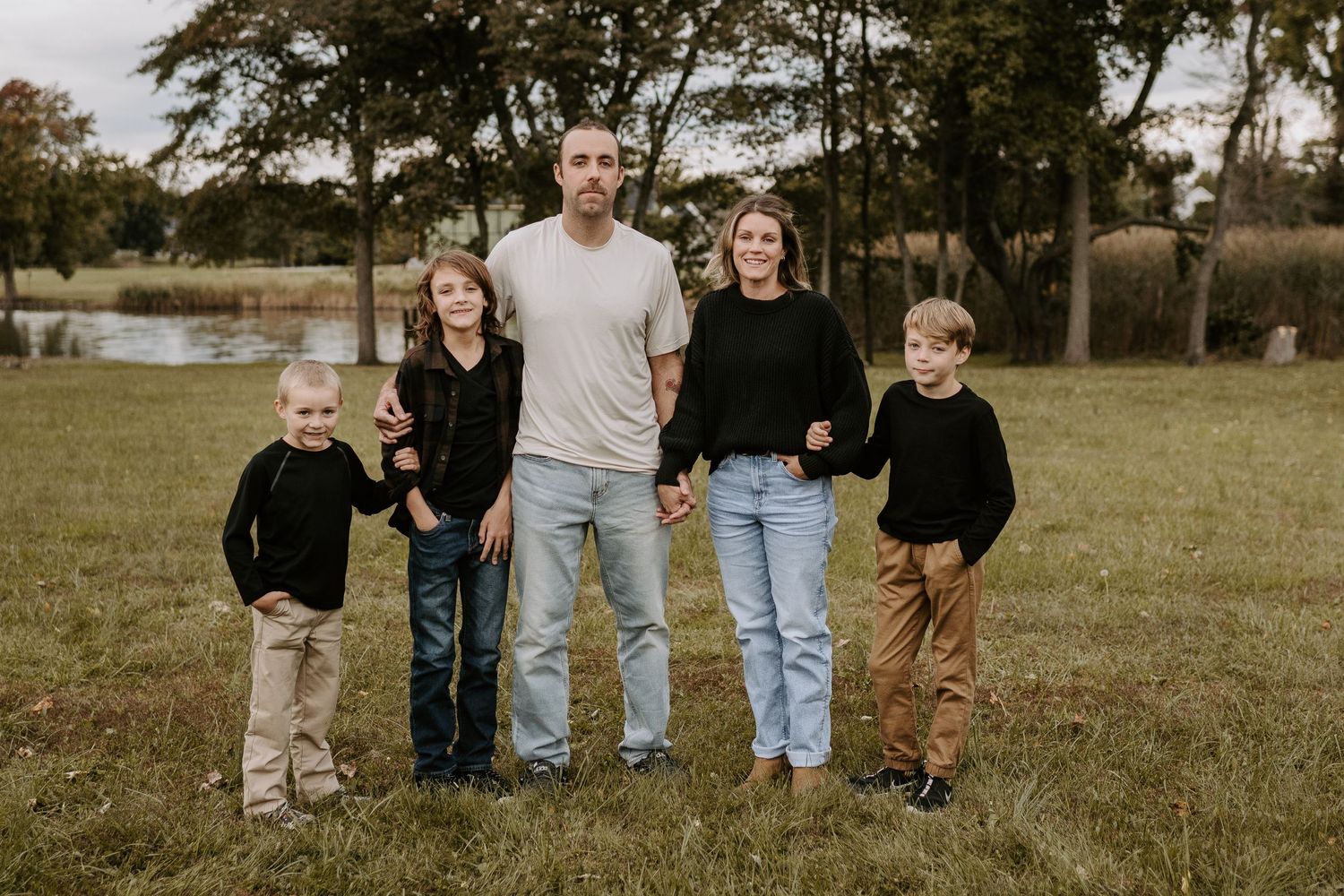 Family of five wearing coordinated casual outfits poses together in an autumn field.