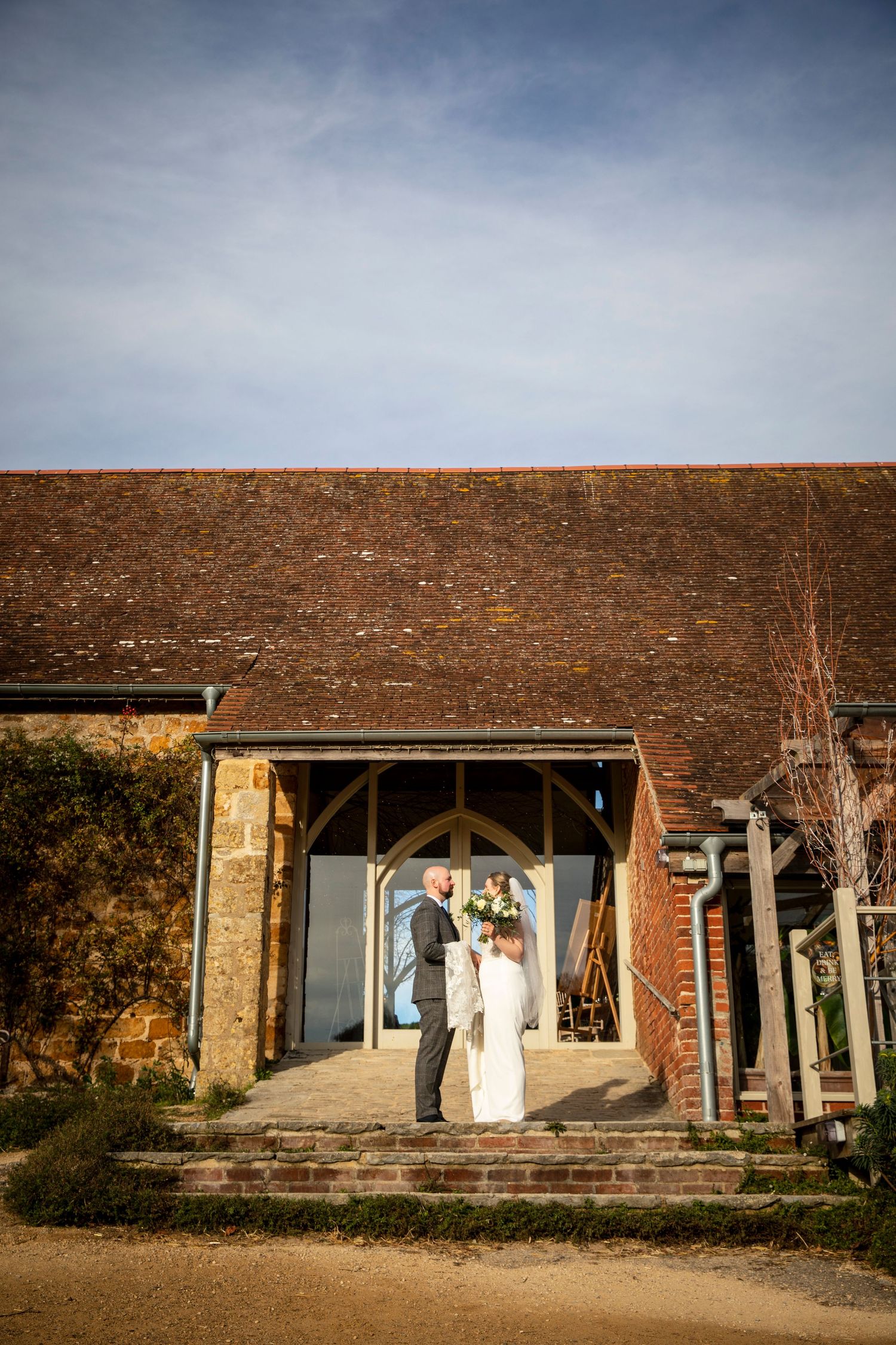 Wedding couple standing in front of a rustic brick building entrance at sunset.