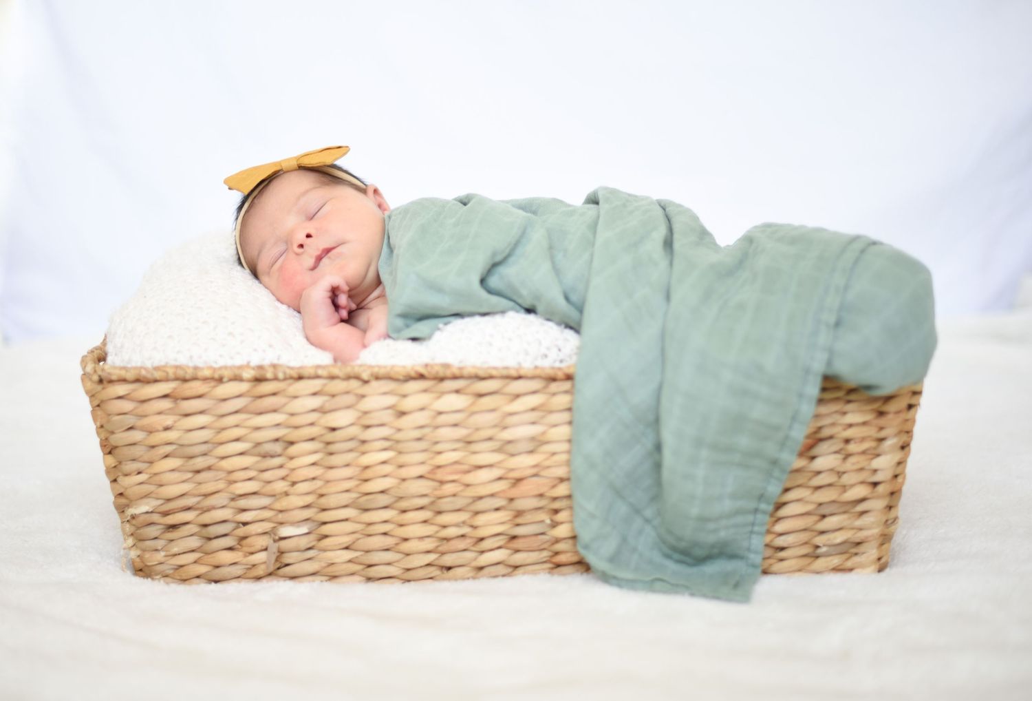Baby in sage green outfit yawning while lying in wicker basket.