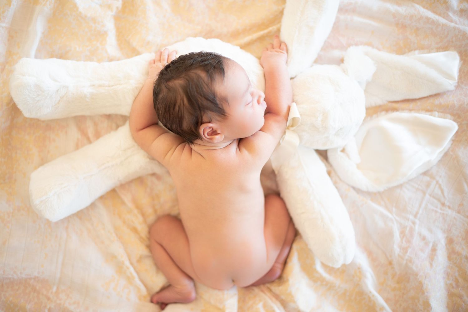 Sleeping newborn on soft white blanket photographed from above.