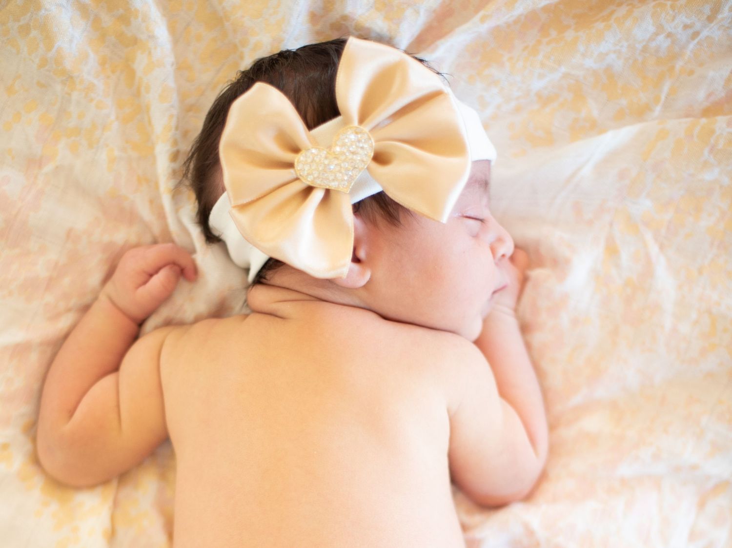 Sleeping newborn wearing a large cream bow headband resting on soft beige fabric.