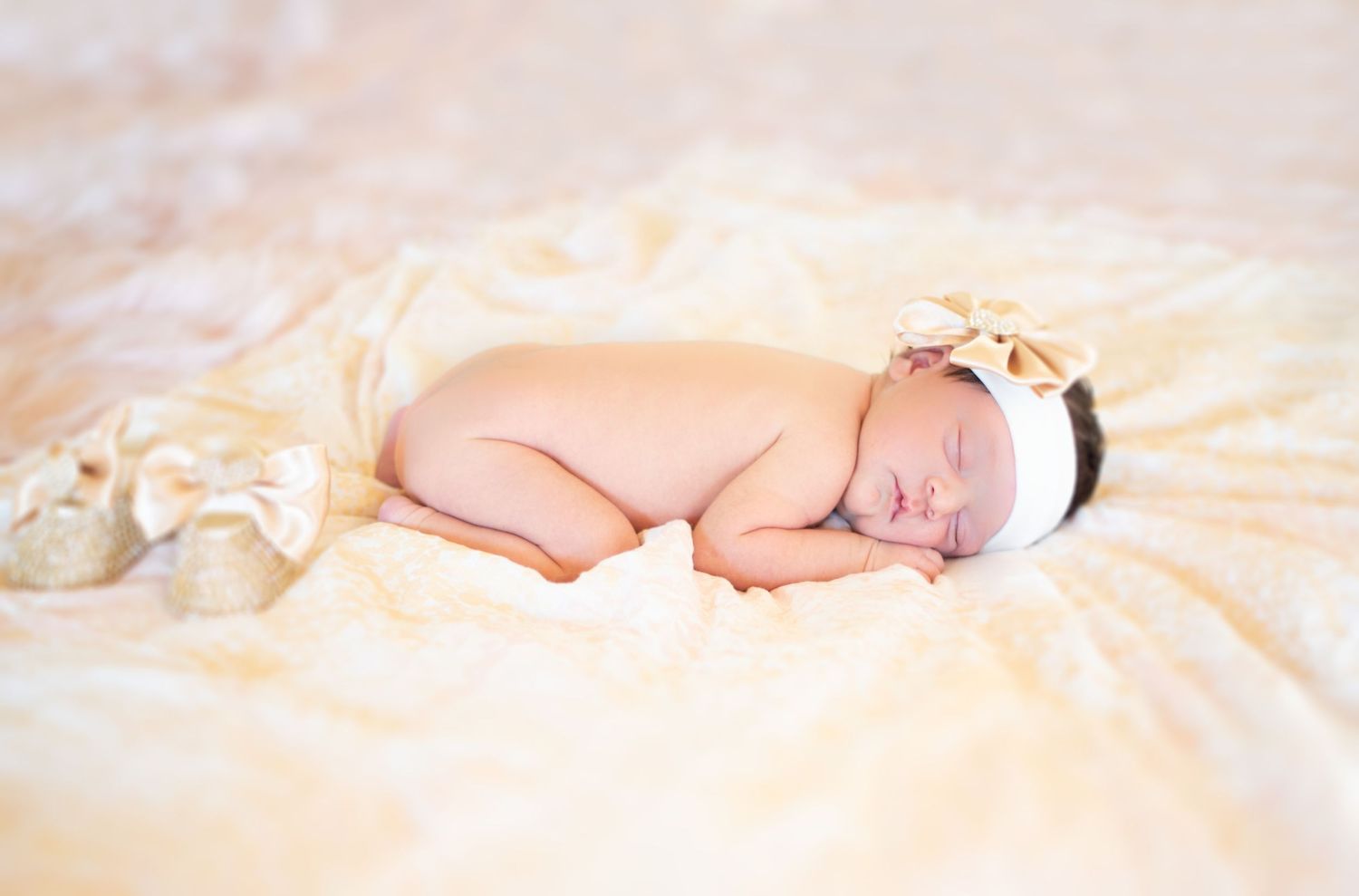 Sleeping newborn with white headband on peachy colored fabric during photo session.