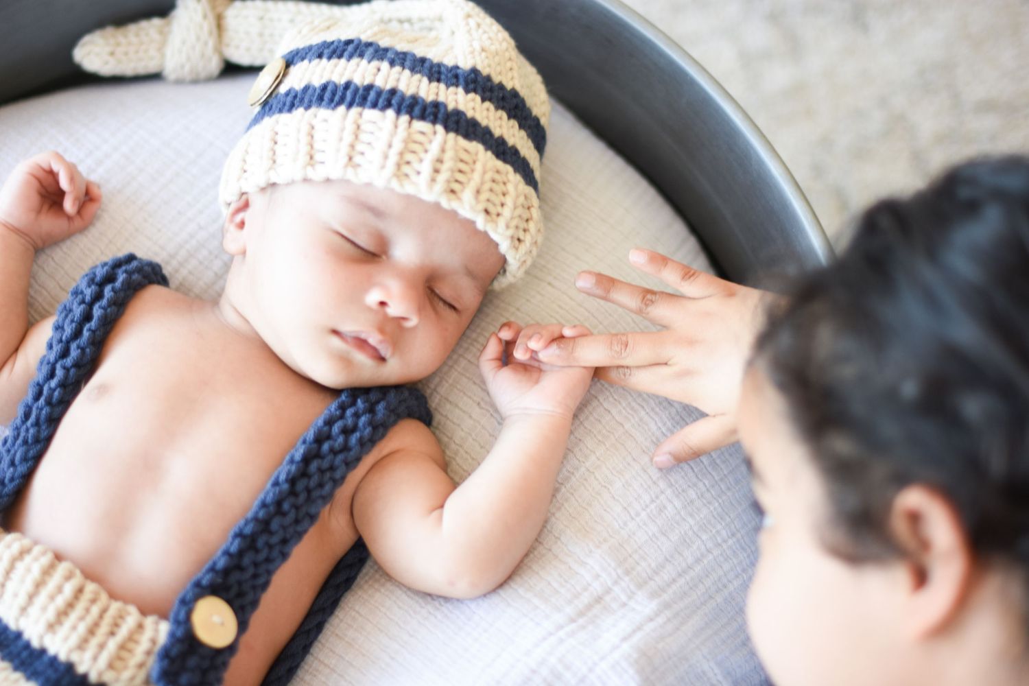 Sleeping newborn wearing knit striped hat being gently touched.