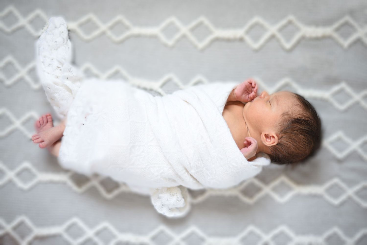 Sleeping newborn wrapped in white lying on gray geometric patterned blanket.