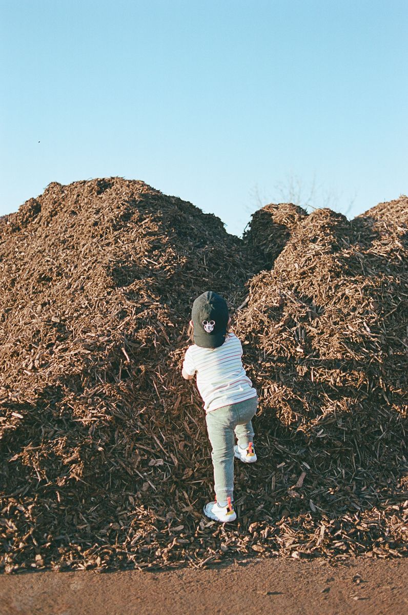 Person in white climbing a large pile of brown material outdoors.