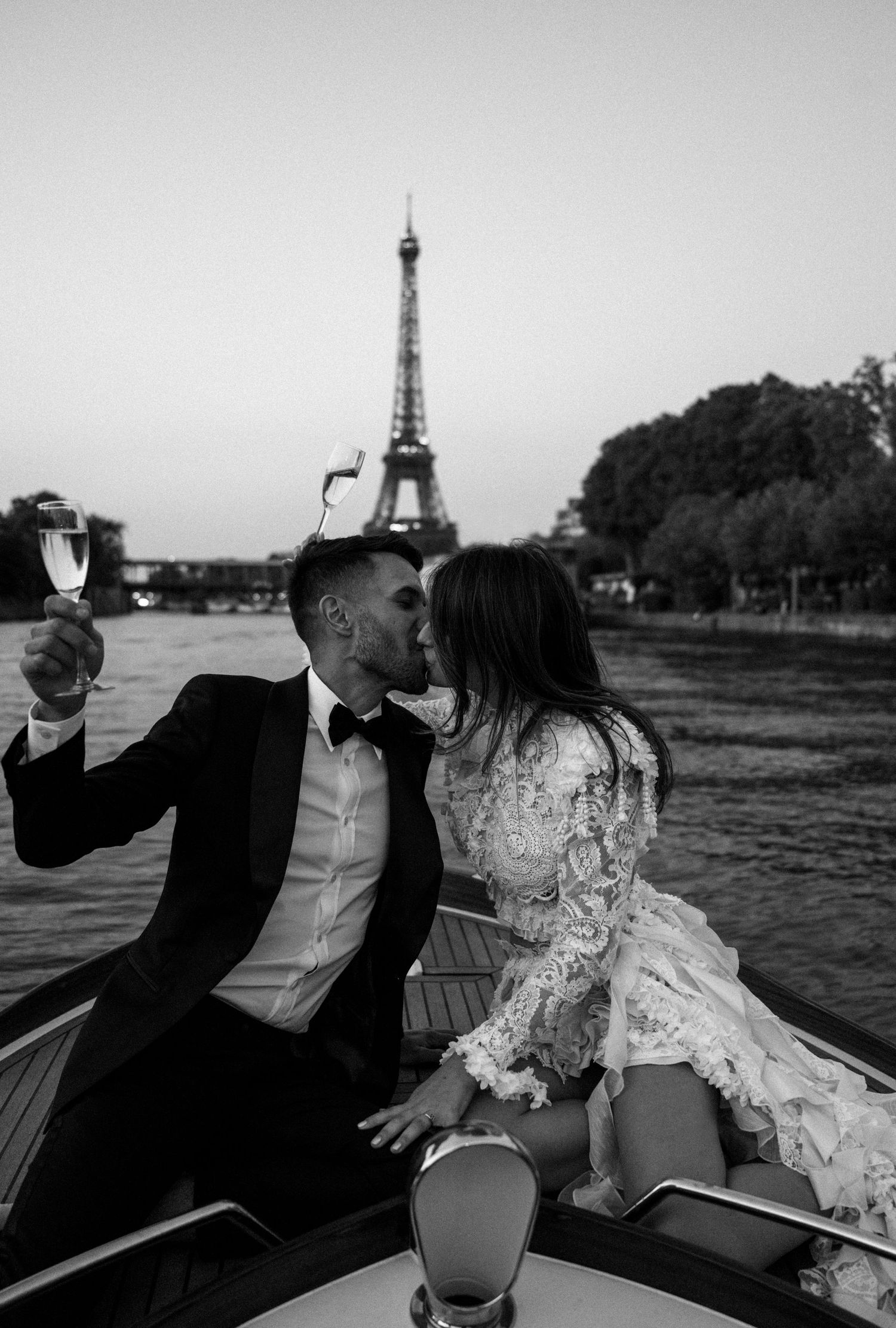 Romantic couple sharing a kiss near the Eiffel Tower in Paris while holding champagne glasses.