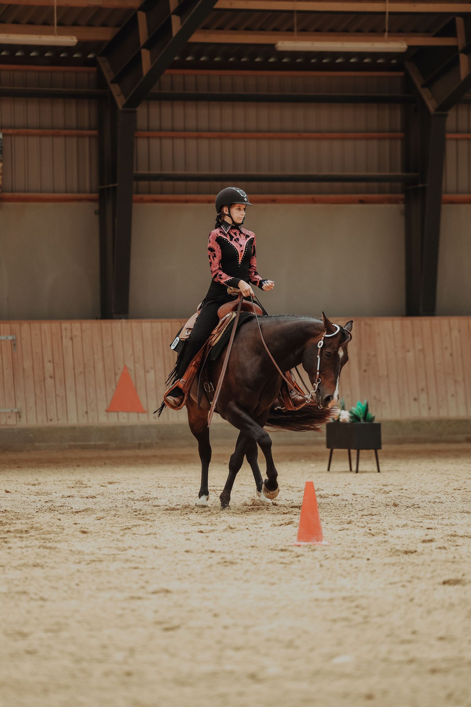 Equestrian navigating orange training cones in an indoor arena setting.