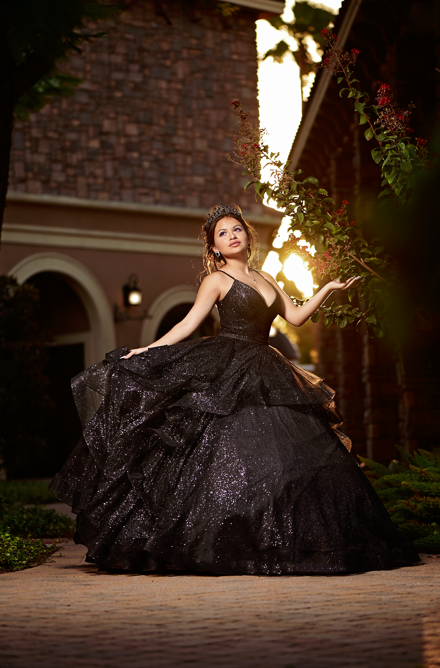 Stunning black ball gown twirls in golden sunset light against architectural backdrop.