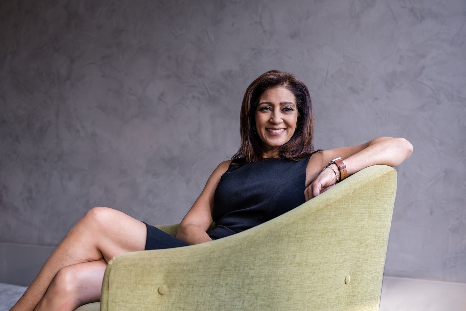 Happy brunette woman wearing black dress sitting in a green. modern chair