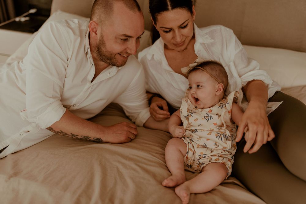 Family lying together on beige couch during an intimate home photo session.
