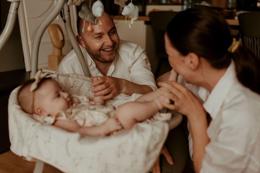 Natural light photography capturing playful family moments on hardwood flooring.
