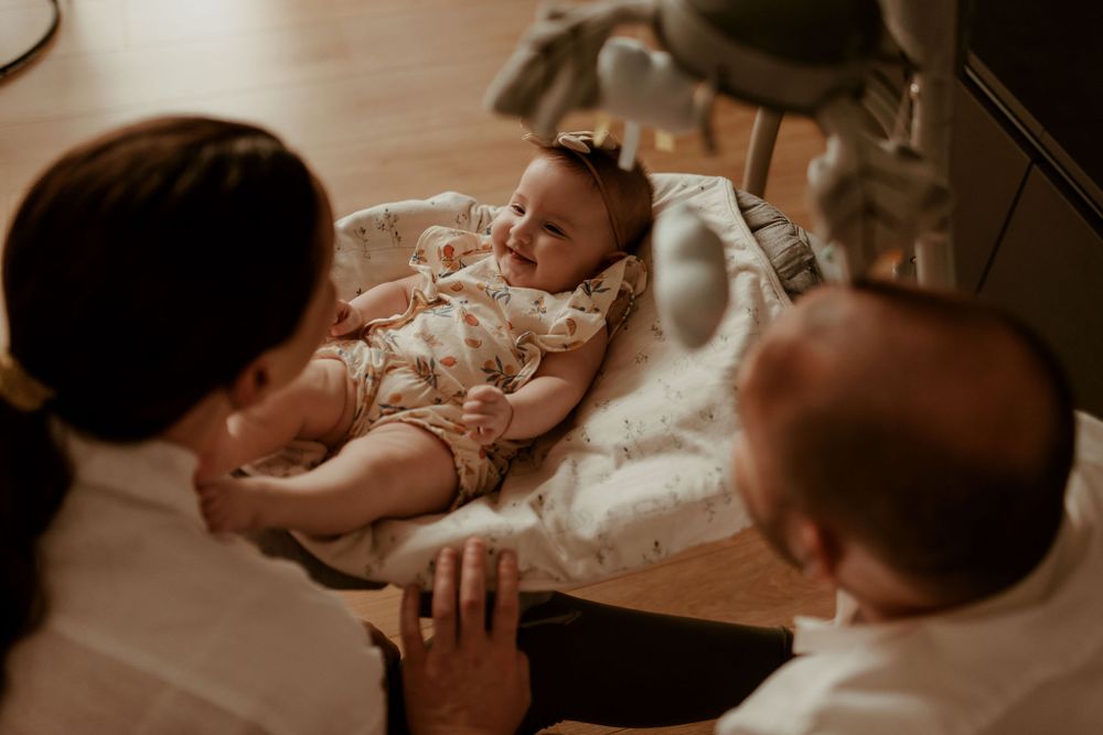 A baby lies on a soft cushioned surface while being lovingly attended to in a warm-toned indoor setting.
