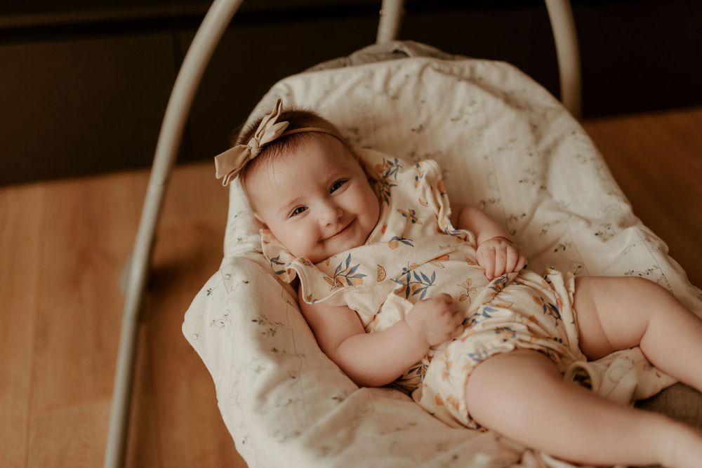 A sleeping baby rests peacefully in a white baby swing wearing a floral outfit.