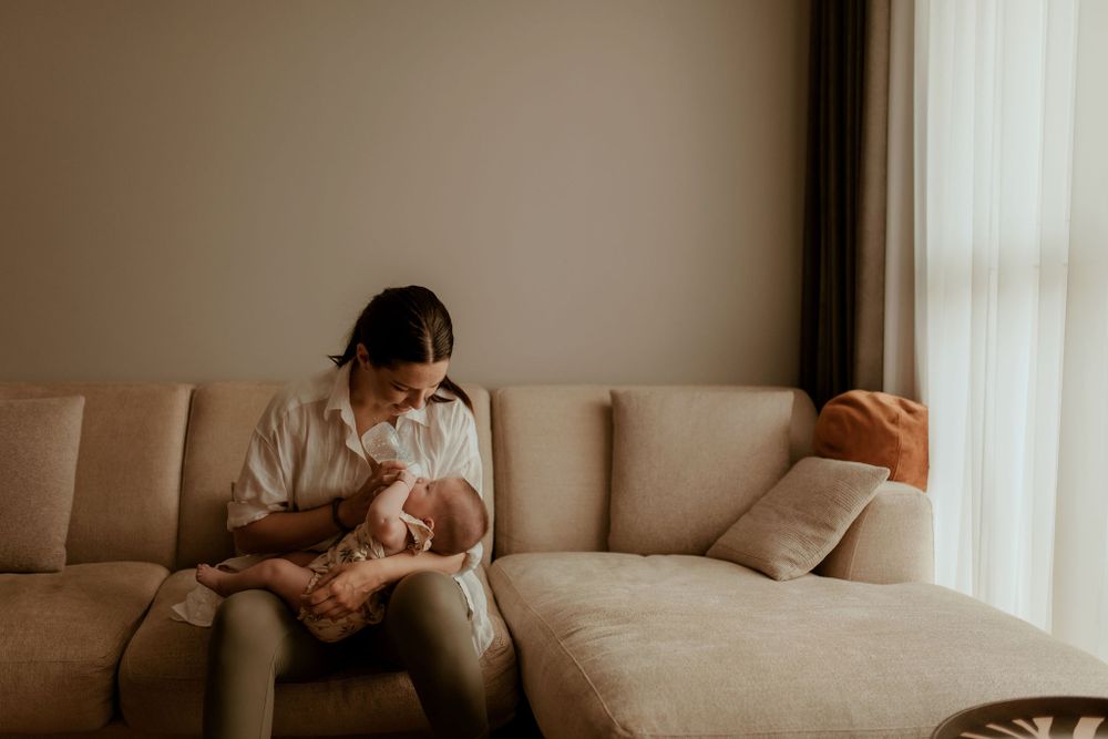 Quiet moment of parent and infant relaxing together on sectional sofa near window.