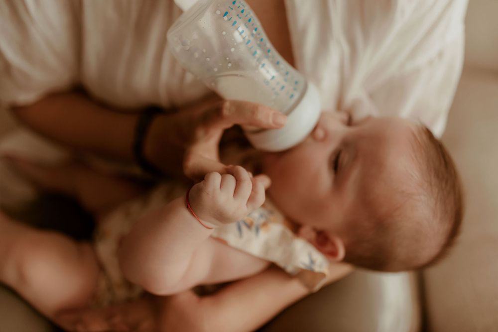 Close-up shot of baby being bottle fed in gentle natural lighting.