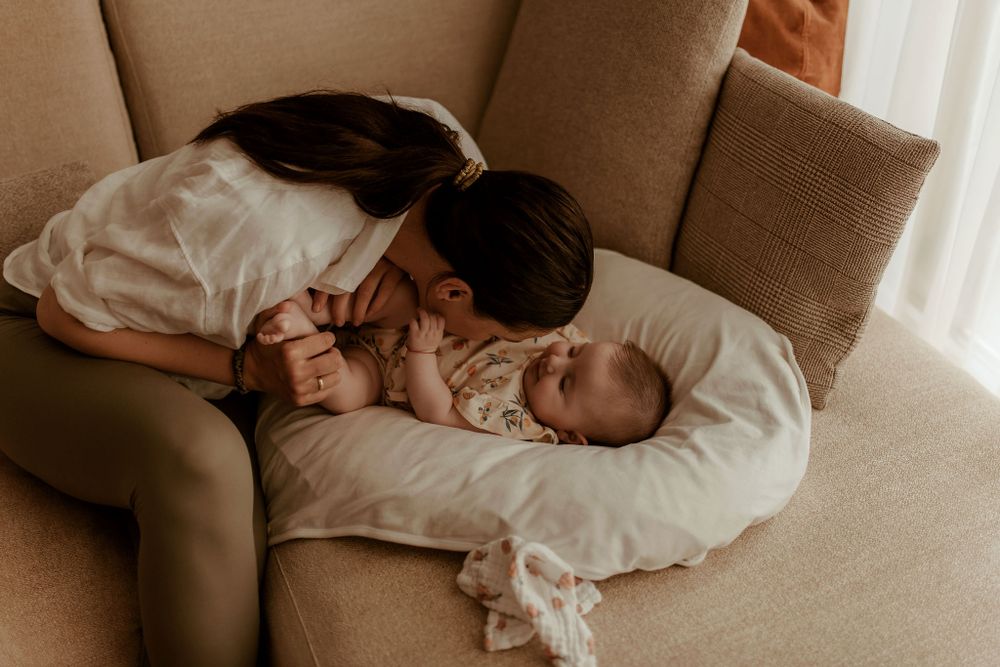 Intimate family moment with baby resting on white pillow on brown couch.