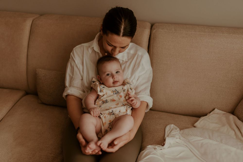 Tender parenting moment on beige couch in warm lighting.