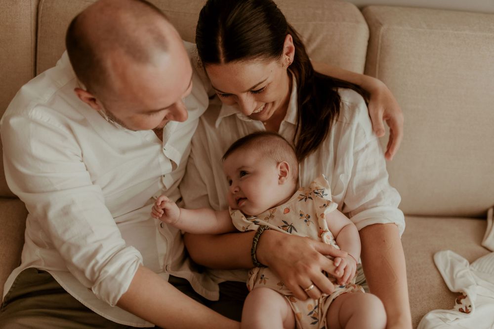 Tender family moment on brown sofa in warm natural light.