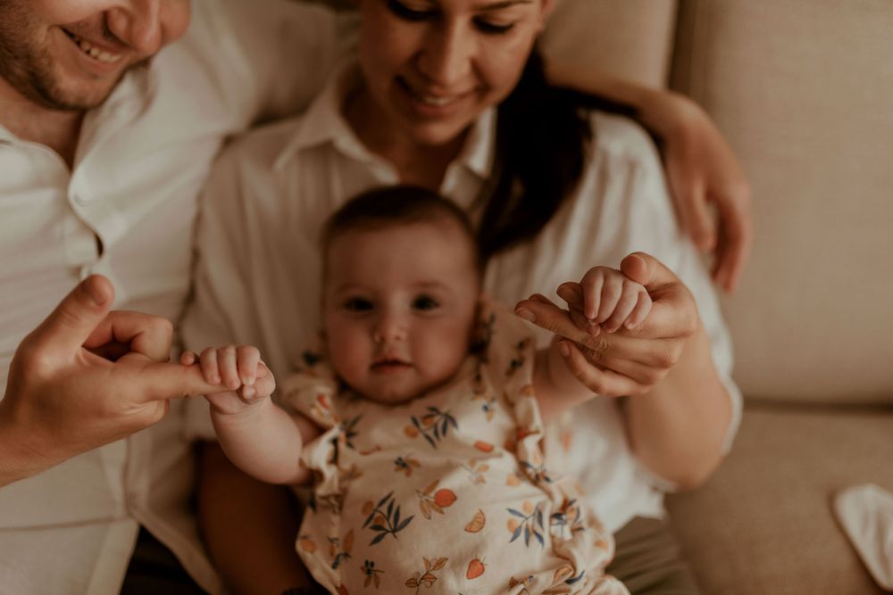 Joyful family interaction with baby in floral outfit on couch.