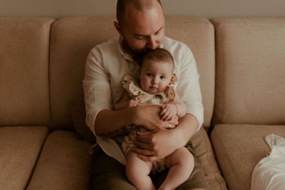Gentle parenting moment on brown sofa in warm lighting.