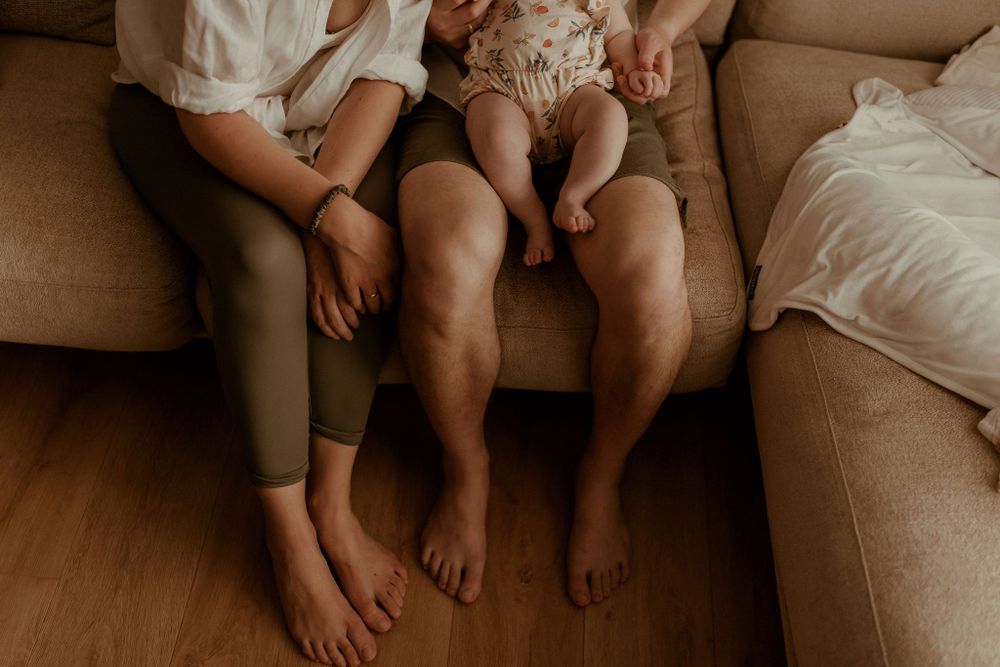 Bare feet of family members resting together on brown couch.