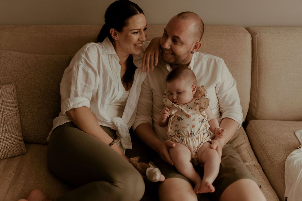 Intimate family portrait session showing tender moments on a beige couch in warm lighting.