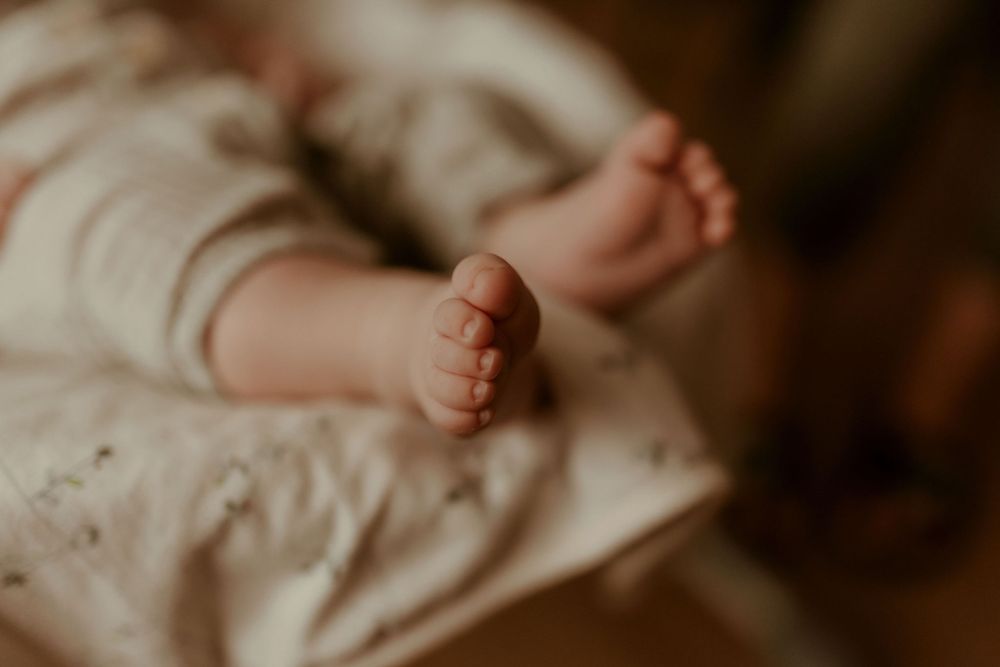 Close-up view of tiny baby feet and hands against neutral beige background.