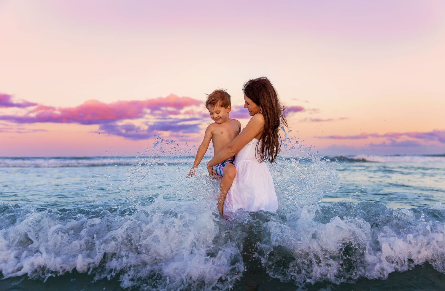 Scenic beach panorama at sunset with pink and purple sky over crashing waves.