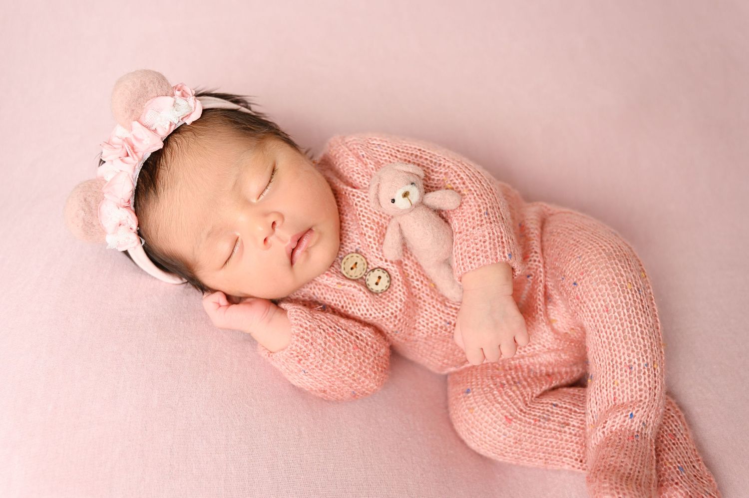 Peaceful newborn photography setup with soft pink knitted outfit and gentle lighting.