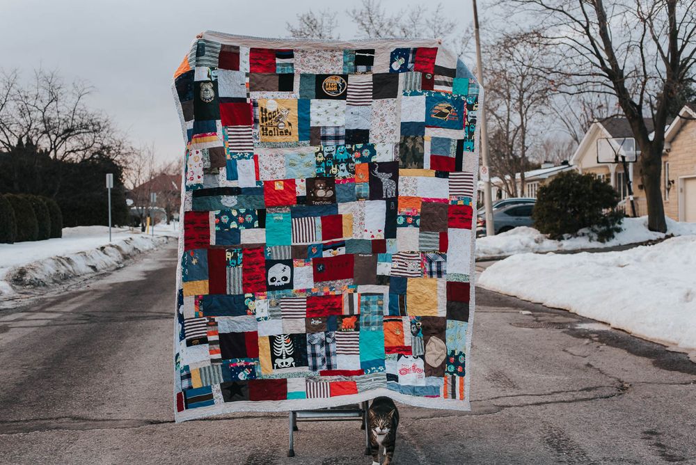 Vibrant memory quilt being held up in the street to be photographed with a cat keenly interested.