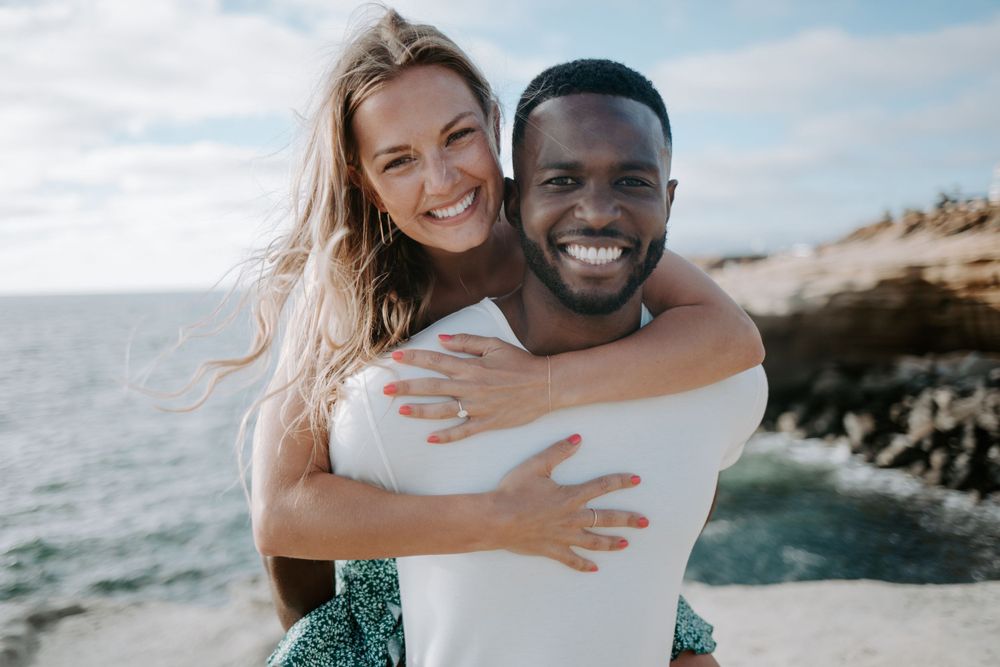 Joyful couple embracing on rocky coastal cliff with ocean view.