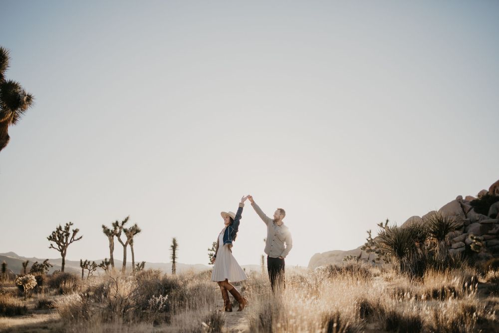 A silhouetted couple dancing in a desert landscape with Joshua trees at sunset.