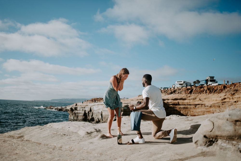 Surprise proposal moment on scenic coastal cliffs overlooking the ocean.
