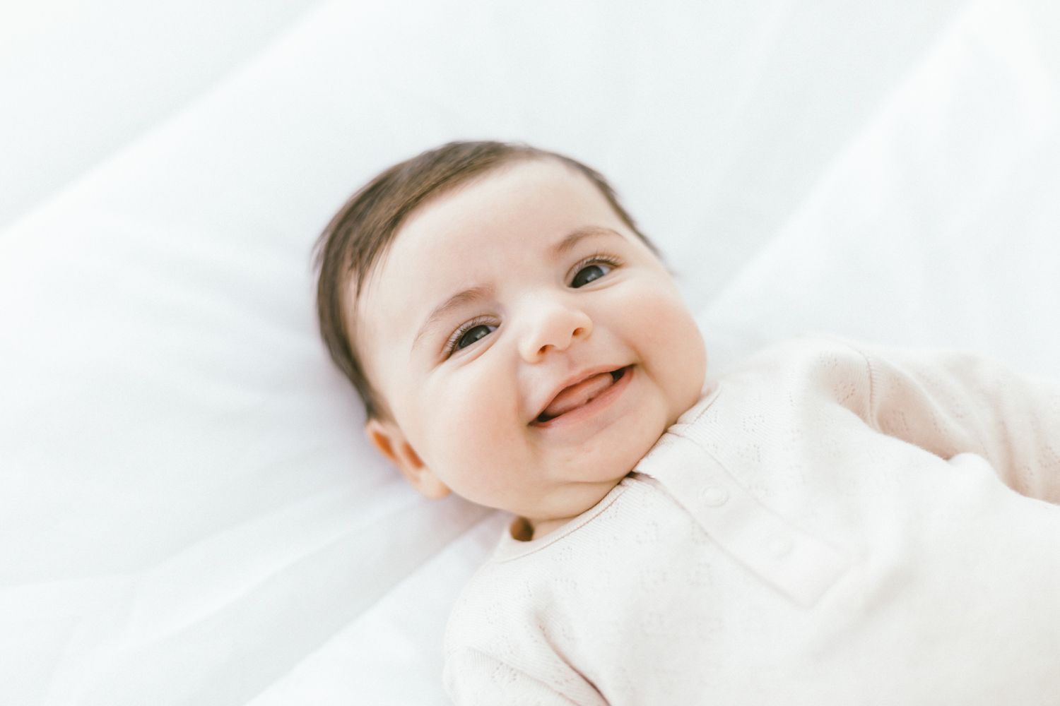 Joyful baby in white outfit smiling on light background.