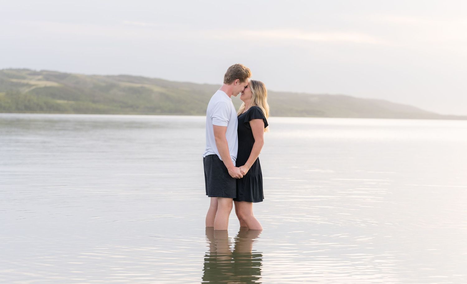 Couple wading in shallow lake water during sunset photoshoot.
