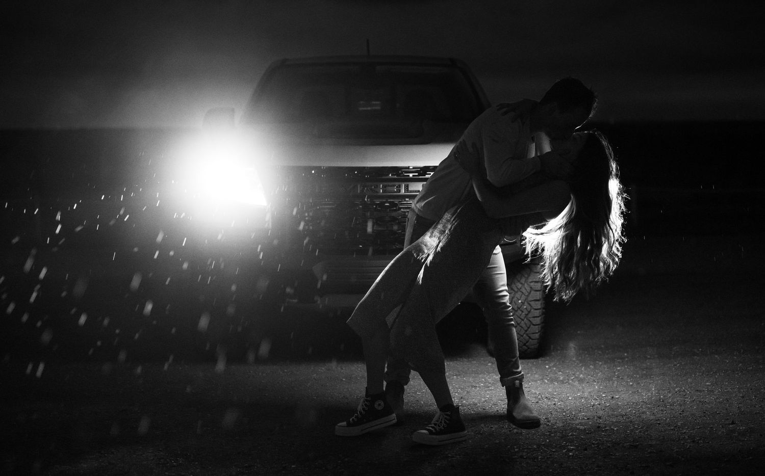 A dramatic black and white shot of a couple dancing in front of car headlights.