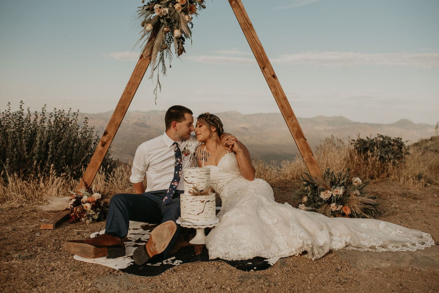 Romantic desert picnic setup with wooden arch and decorations.