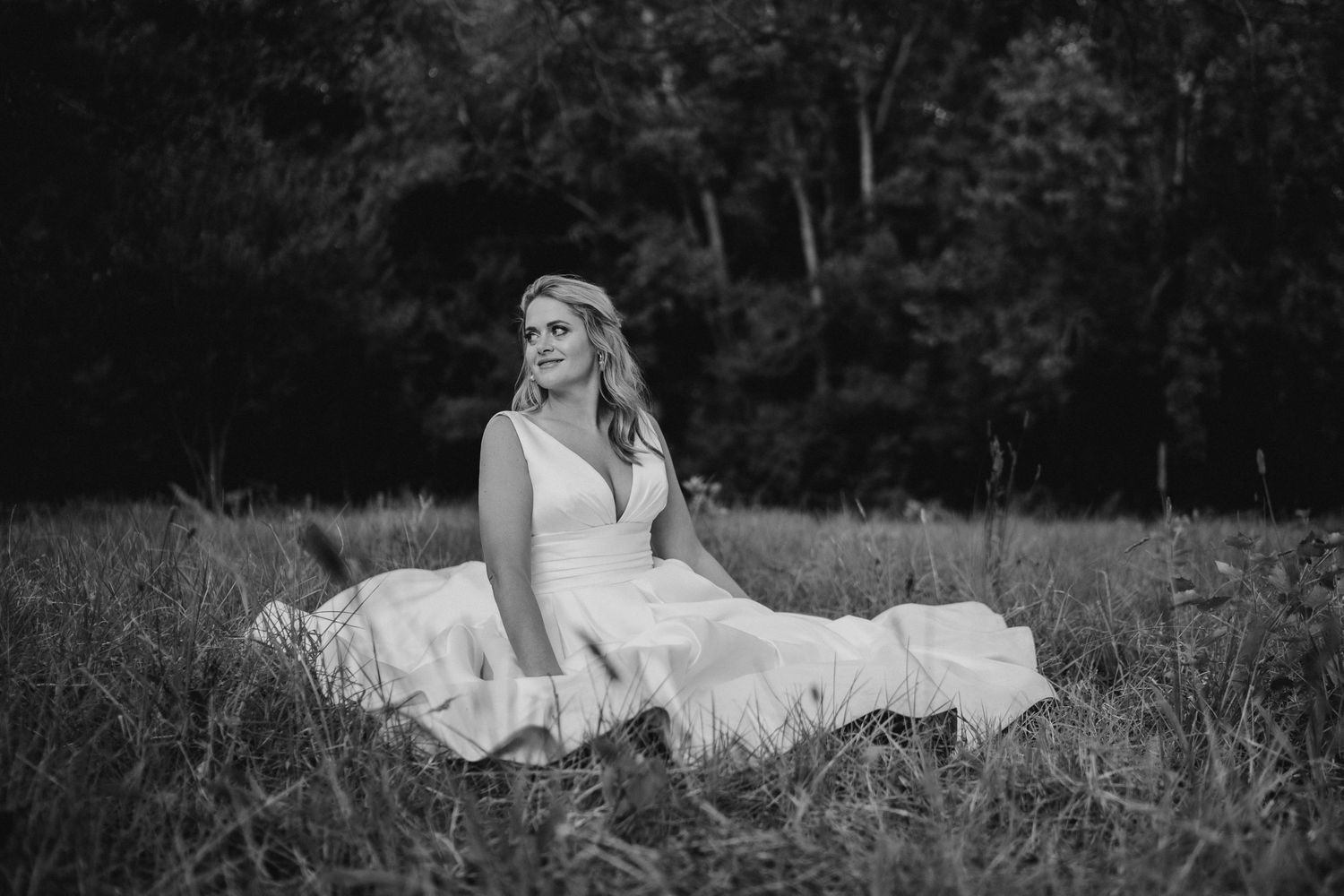 A black and white portrait of someone in a wedding dress sitting in a meadow.