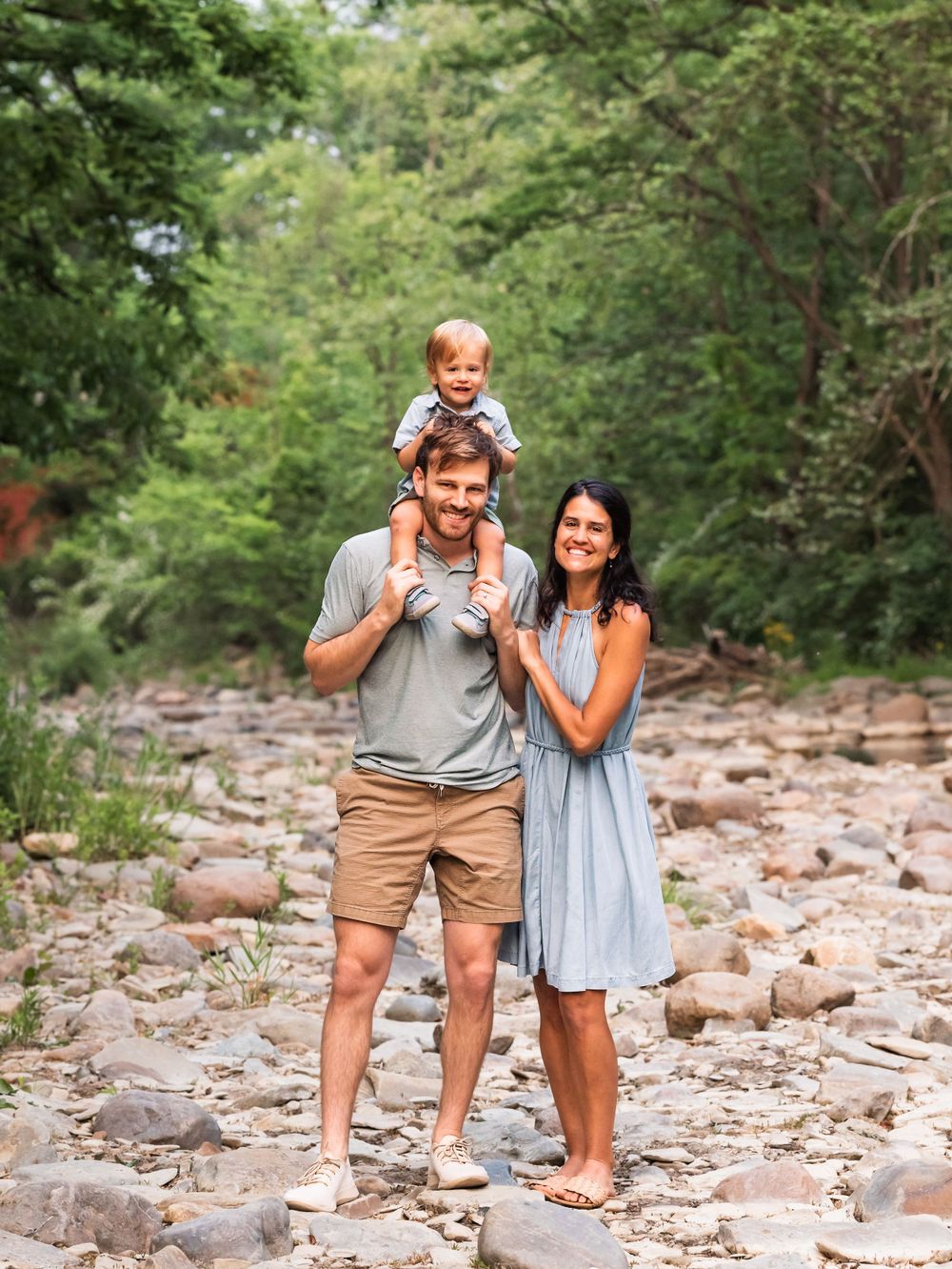 Outdoor summer family picture of toddler and parents in riverbed of rocks
