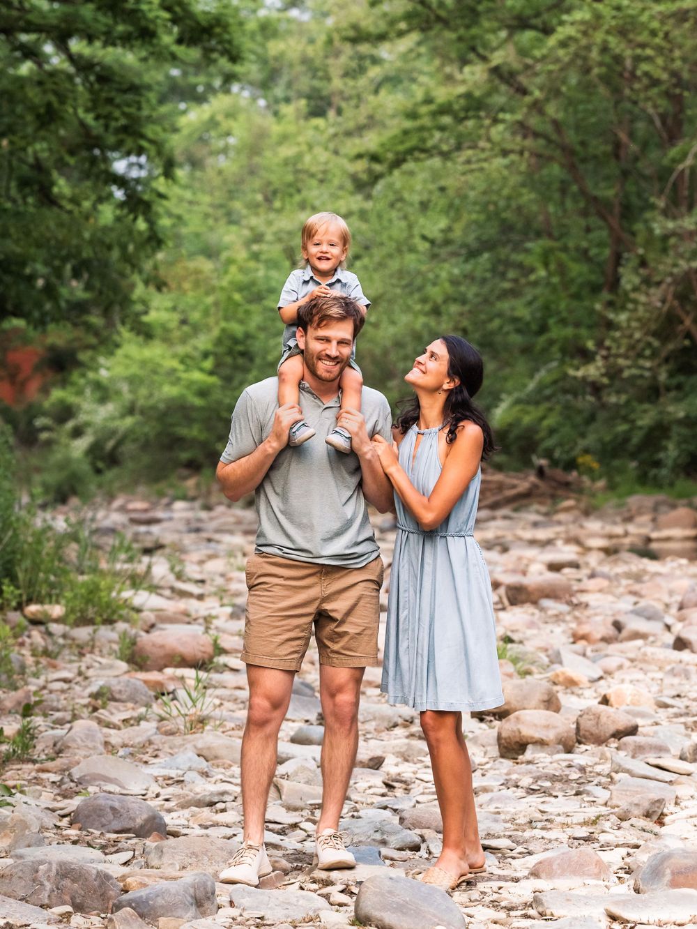 Family of three summer photo session of mother looking up at baby boy on dad's shoulders