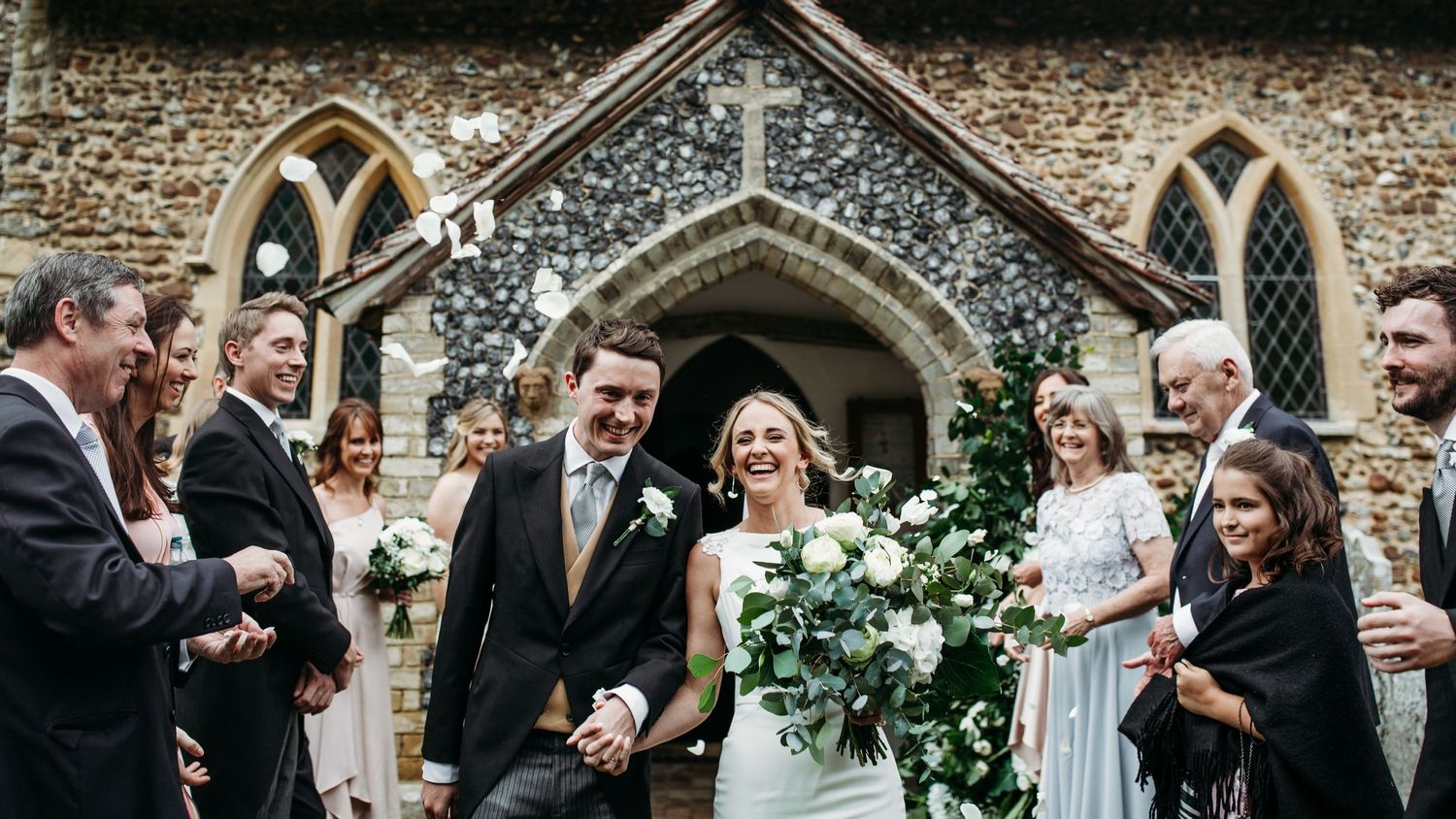 Celebratory wedding party gathered outside a historic stone church with Gothic arched doorway.