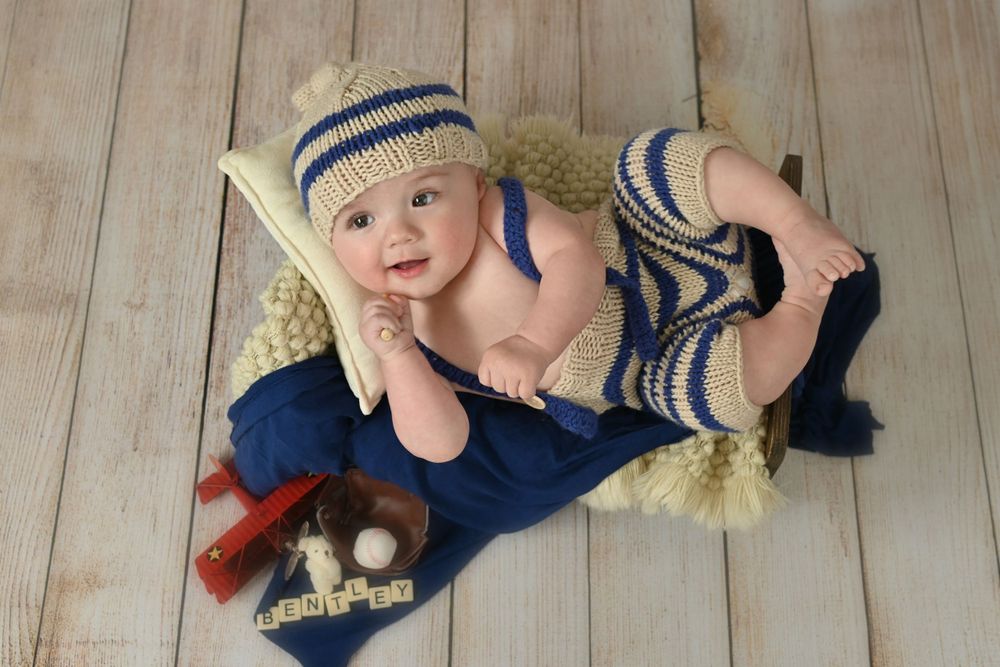 Baby in blue striped knit outfit lying on soft blanket with baseball accessories.