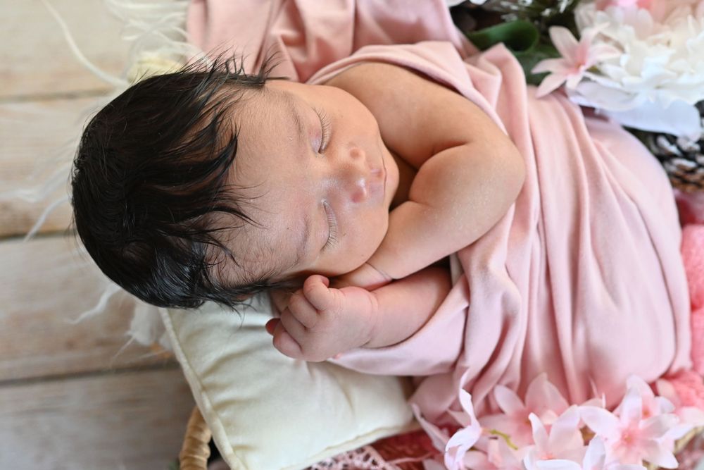 Sleeping newborn wrapped in pink fabric resting peacefully on white pillow.