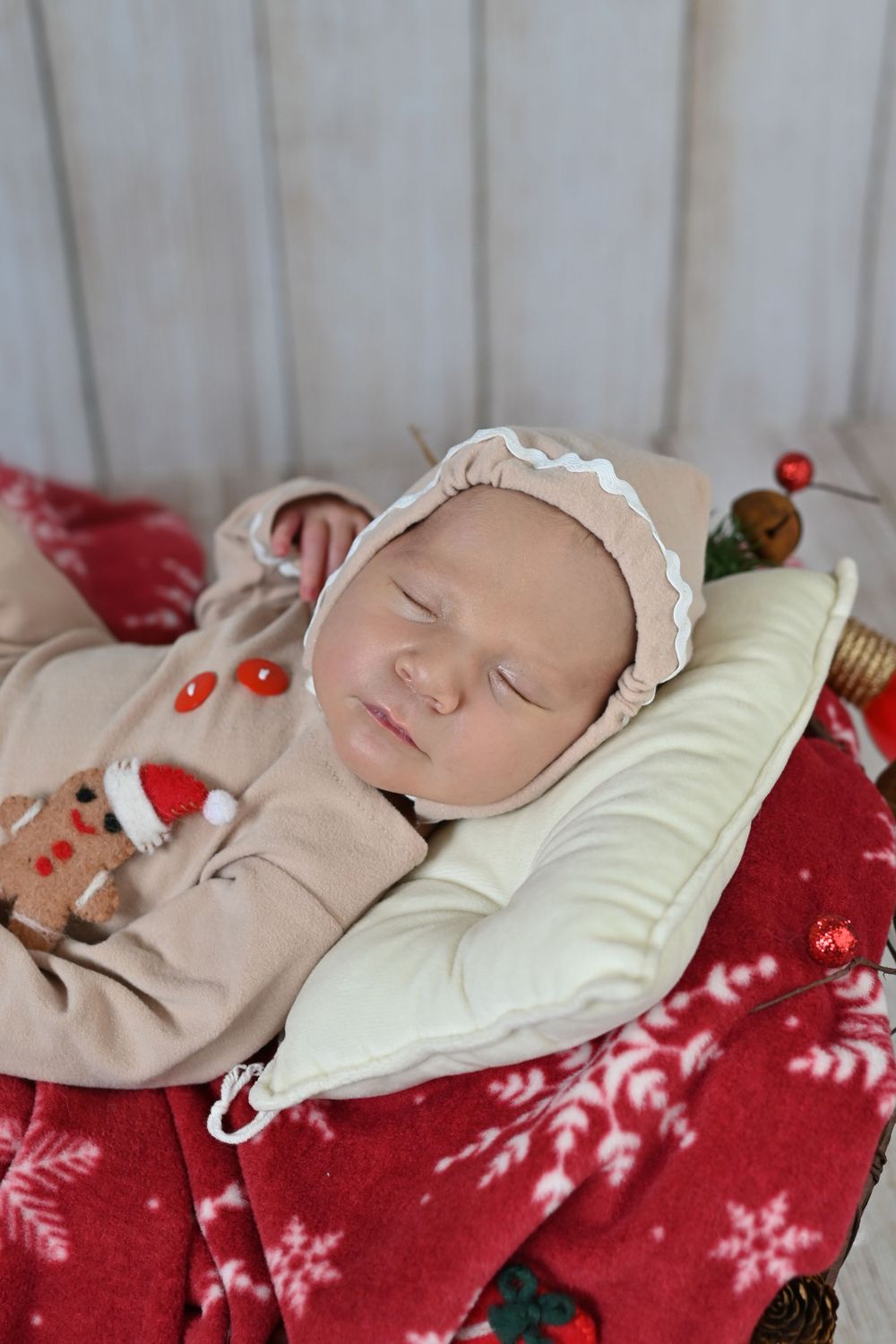 Baby sleeps on red snowflake blanket with festive decorations.
