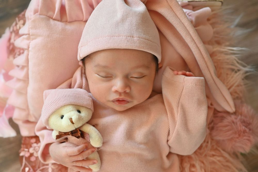 Sleeping newborn in soft pink knit wrap with delicate accessories.