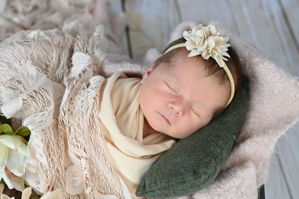 Sleeping newborn wearing cream headband and lace wrap on soft blanket.